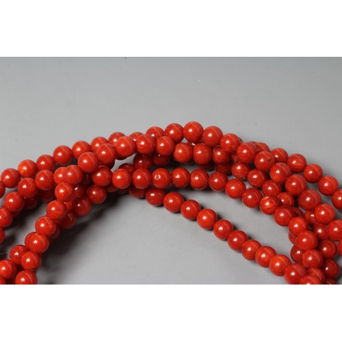 201 - A SIX STRAND CORAL BEAD BRACELET, the strands set into a crescent shaped panel clasp chased with scr... 