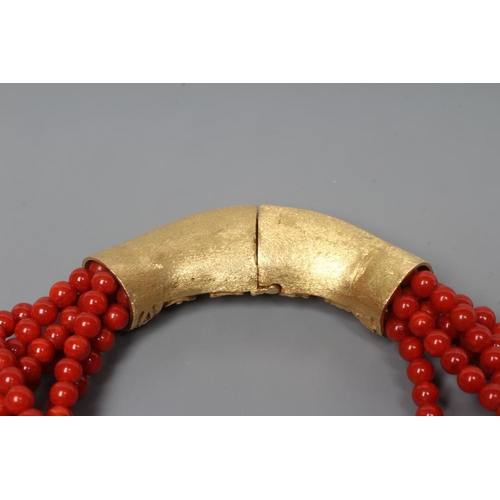 201 - A SIX STRAND CORAL BEAD BRACELET, the strands set into a crescent shaped panel clasp chased with scr... 