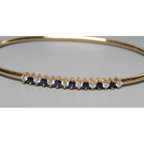 232 - A STIFF HINGED BANGLE, the upper section claw set with seven small sapphires and eight diamonds, to ... 