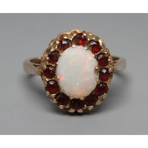 244 - AN OPAL AND GARNET CLUSTER RING, the oval cabochon polished opal claw set to a border of small facet... 