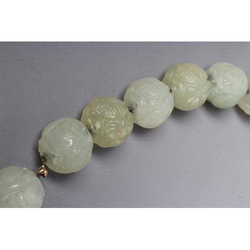 253 - A STRING OF CHINESE CELADON JADE BEADS, the forty six spherical beads carved with scroll and flowers... 