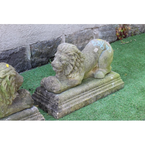 547 - A PAIR OF CAST STONE RECUMBENT LIONS each holding a ball in its front paws, on moulded oblong base, ... 