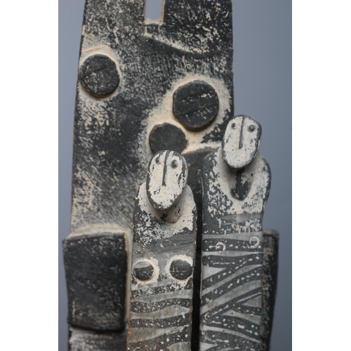 81 - JOHN MALTBY (1936-2000) - a matt grey stoneware sculpture of two figures standing before a cut slab ... 