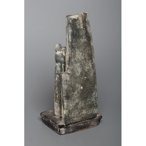 81 - JOHN MALTBY (1936-2000) - a matt grey stoneware sculpture of two figures standing before a cut slab ... 