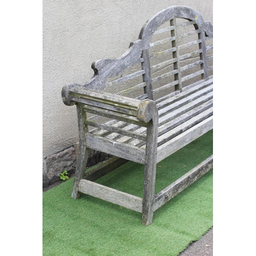 736 - A LUTYENS STYLE SLATTED TEAK GARDEN BENCH with arched back and scrolled arms, raised on square secti... 