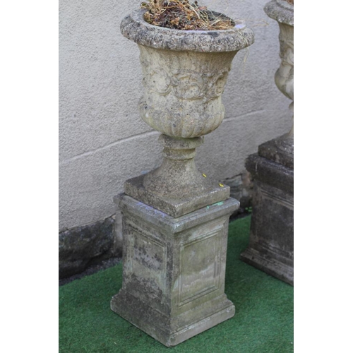 738 - A PAIR OF CAST STONE URNS of half fluted campana form with ovolu moulded rim, a band of foliate scro... 