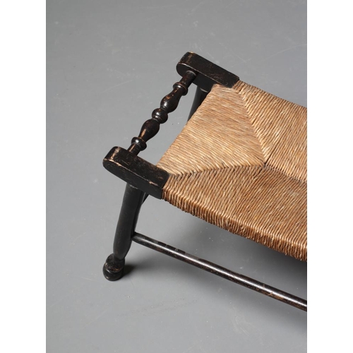 844 - AN ARTS AND CRAFTS EBONISED RUSH SEATED STOOL, late 19th century, the oblong dished seat with balust... 