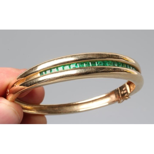 177 - AN EMERALD STIFF HINGED BANGLE, the upper section channel set with twenty two graduated calibre squa... 