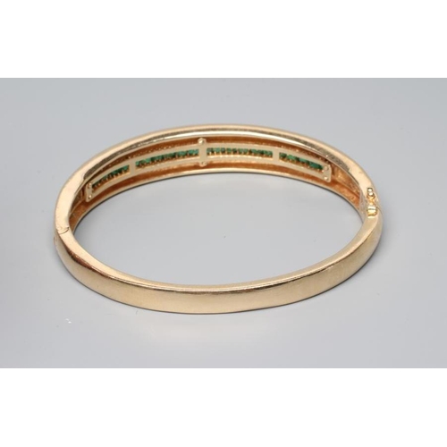 177 - AN EMERALD STIFF HINGED BANGLE, the upper section channel set with twenty two graduated calibre squa... 