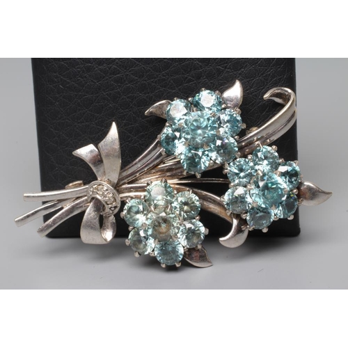 196 - A BLUE TOPAZ TRIPLE FLOWER SPRAY BROOCH, the nine stone flowerhead clusters set to a white frame wit... 