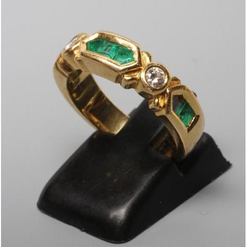 243 - AN EMERALD AND DIAMOND HALF HOOP RING, the heavy cast panel centred by three channel cut emeralds fl... 