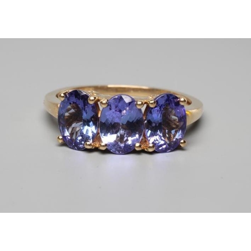 263 - A THREE STONE TANZANITE RING, the oval facet cut stones claw set to a plain shank, stamped 14k, 585,... 