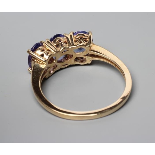 263 - A THREE STONE TANZANITE RING, the oval facet cut stones claw set to a plain shank, stamped 14k, 585,... 