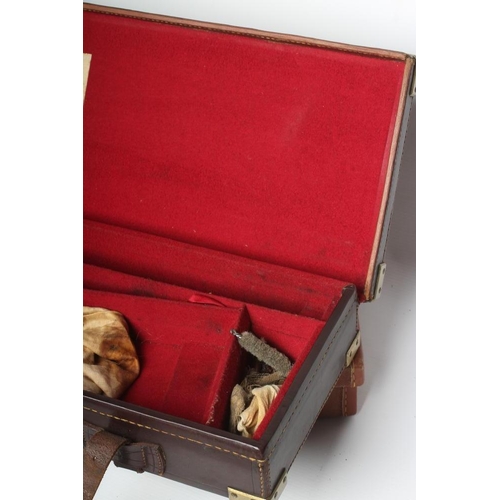 597 - TWO GUN CASES, comprising a leather example, with brass furniture, red interior baize and label for ... 