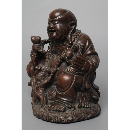 653 - A CHINESE CARVED HARDWOOD BUDDAH, seated wearing a long bead necklace and with three children in att... 