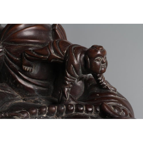 653 - A CHINESE CARVED HARDWOOD BUDDAH, seated wearing a long bead necklace and with three children in att... 