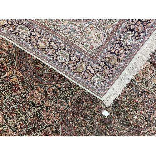 687 - A PERSIAN SILK RUG, the pale green floral field with four oval guls with exotic birds, within an ind... 