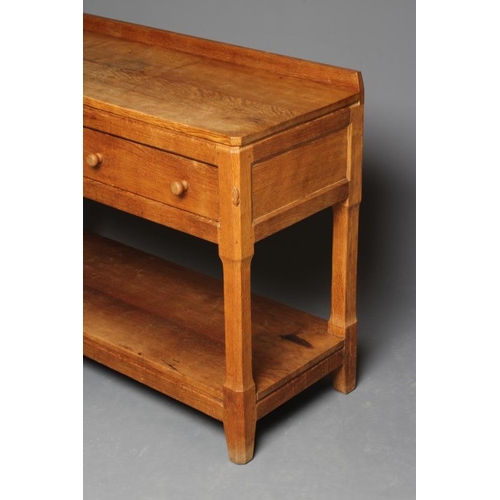 885 - A PETER HEAP ADZED OAK SIDE TABLE, the moulded edged canted oblong top with ledge back, two frieze d... 