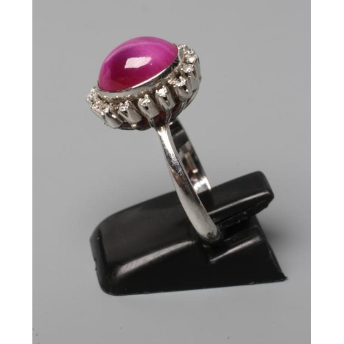 448 - A STAR RUBY AND DIAMOND RING, the oval cabochon ruby collet set to a border of sixteen small diamond... 