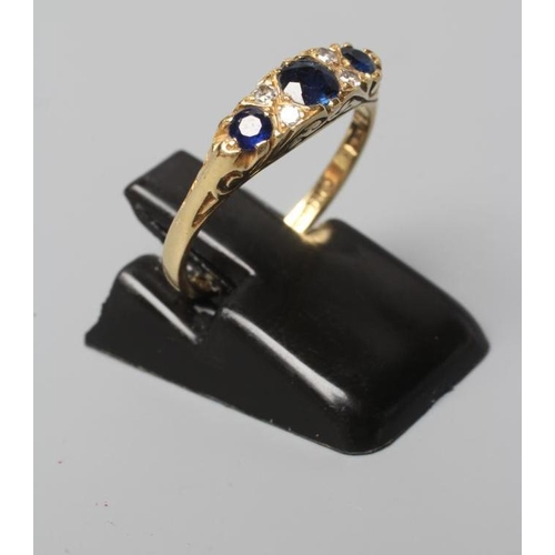 500 - A SEVEN STONE SAPPHIRE AND DIAMOND RING, with carved scroll shoulders and plain 18ct gold shank, Bir... 