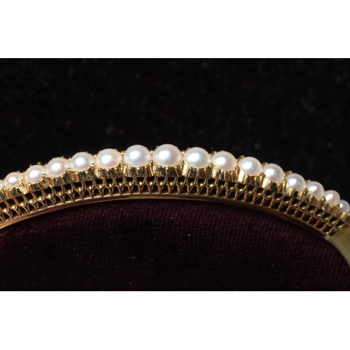 515 - AN EDWARDIAN STIFF HINGED BANGLE, the upper section with nineteen graduated pearls to a plain, unmar... 