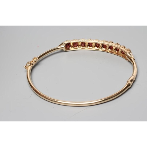 305 - A STIFF HINGED BANGLE, the upper section claw set with ten oval facet cut garnets, indistinctly stam... 