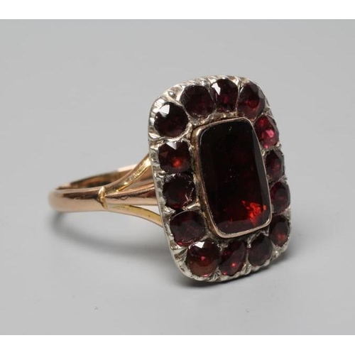 315 - AN EARLY VICTORIAN GARNET CLUSTER RING, the central trap cut stone within a border of fourteen mix c... 