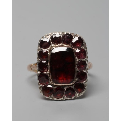 315 - AN EARLY VICTORIAN GARNET CLUSTER RING, the central trap cut stone within a border of fourteen mix c... 