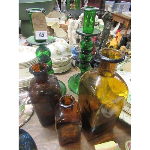 83 - THREE BROWN GLASS BOTTLES AND TWO GREEN GLASS CANDLESTICKS