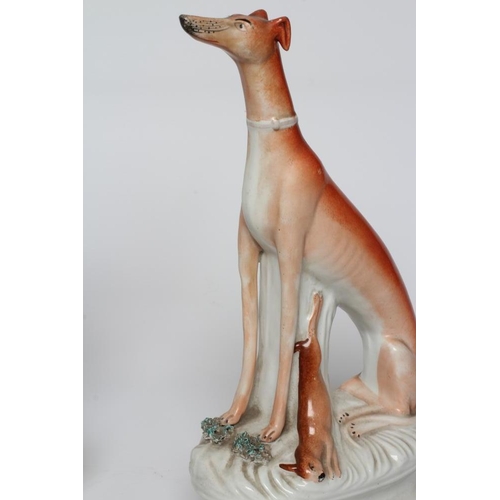 19 - A PAIR OF VICTORIAN STAFFORDSHIRE POTTERY GREYHOUNDS modelled seated with free-standing fore-legs, h... 