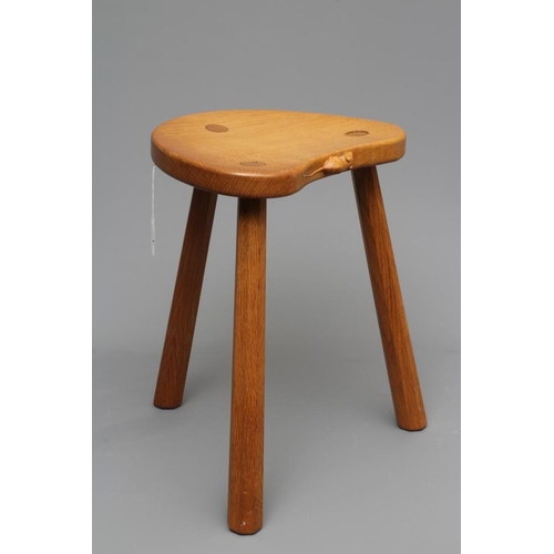 649 - A ROBERT THOMPSON ADZED OAK COW STOOL, the mildly dished kidney shaped top raised on three faceted s... 