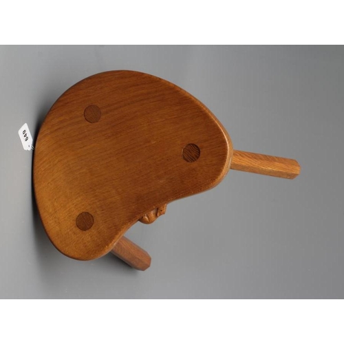 649 - A ROBERT THOMPSON ADZED OAK COW STOOL, the mildly dished kidney shaped top raised on three faceted s... 