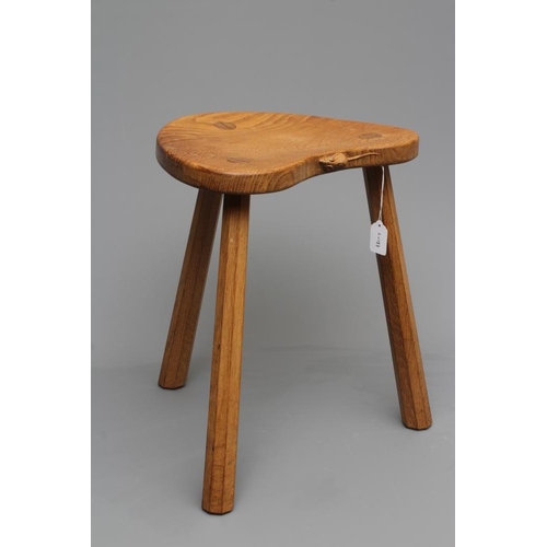 653 - A ROBERT THOMPSON ADZED OAK COW STOOL, the dished kidney shaped top raised on three faceted splayed ... 