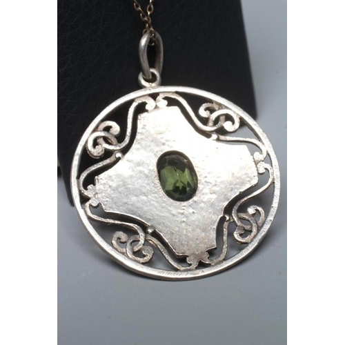 320 - AN ARTS AND CRAFTS CIRCULAR PEWTER PENDANT, centred by an oval facet cut green stone in a planished ... 