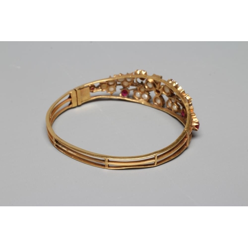 341 - A LATE VICTORIAN STIFF HINGED BANGLE, the open upper section set with seven rubies and numerous cult... 