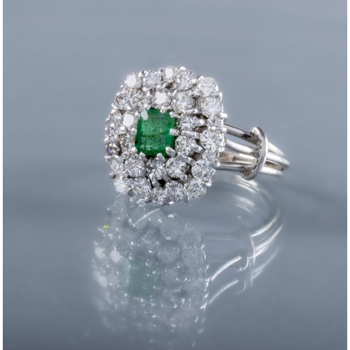 392 - AN EMERALD AND DIAMOND CLUSTER COCKTAIL RING, the central oval facet cut emerald claw set to a doubl... 