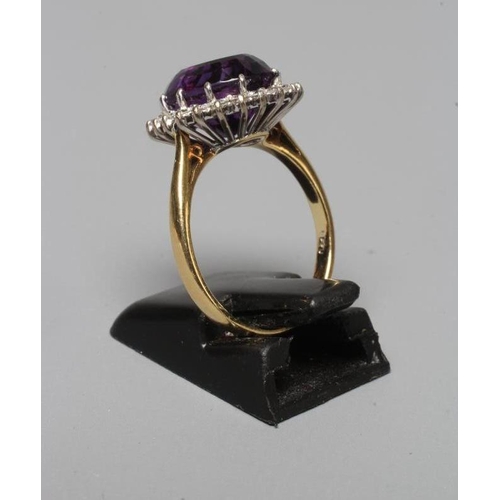 214 - AN AMETHYST AND DIAMOND CLUSTER RING, the central oval facet cut amethyst claw set to a border of tw... 