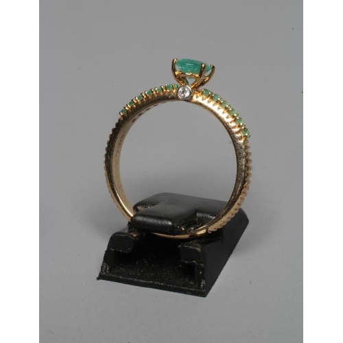 227 - AN EMERALD DRESS RING, the central oval facet cut stone high claw set with a small diamond to each e... 