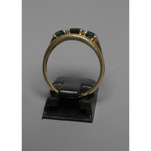 235 - A THREE STONE GREEN TOURMALINE RING, the circular facet cut stones claw set to open shoulders and a ... 