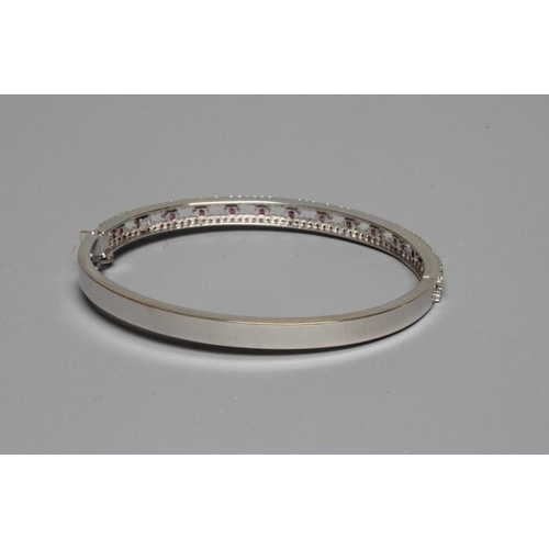 240 - A 9CT WHITE GOLD STIFF HINGED BANGLE, the open upper section set with fourteen small square cut rubi... 