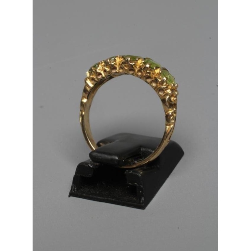 261 - A FIVE STONE PERIDOT RING, the oval and circular facet cut stones set to scroll carved shoulders and... 