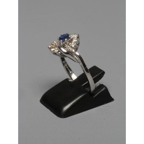 262 - A SAPPHIRE AND DIAMOND ABSTRACT CLUSTER RING, the circular facet cut sapphire claw set to a semi-who... 