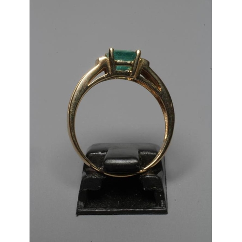 295 - AN EMERALD RING, the oblong facet cut stone claw set between shoulders each pave set with two diamon... 