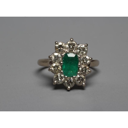 311 - AN EMERALD AND DIAMOND CLUSTER RING, the oblong facet cut emerald claw set within a border of ten br... 