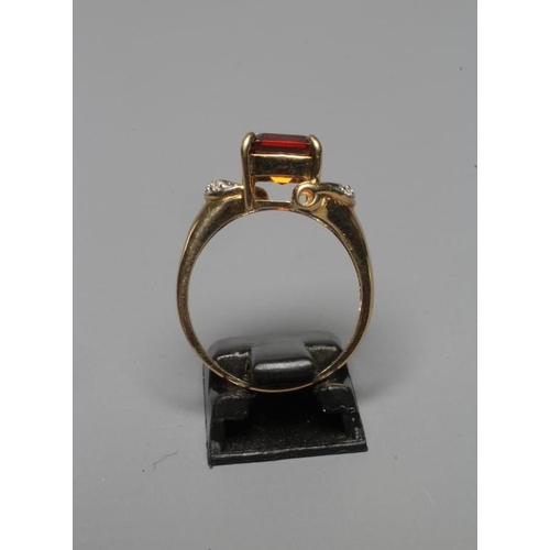 319 - A DRESS RING, the claw set square cut garnet between open horseshoe shoulders each pave set with thr... 