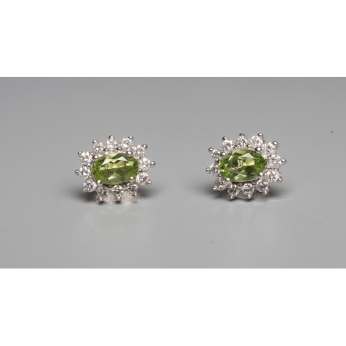 292 - A PAIR OF PERIDOT AND DIAMOND EAR STUDS, the oval facet cut peridots set to a border of twelve point... 