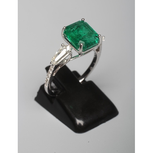313 - AN EMERALD DRESS RING, the octagonal cut stone of 3.18cts claw set to shoulders each further set wit... 