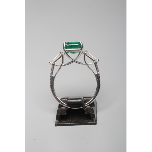 313 - AN EMERALD DRESS RING, the octagonal cut stone of 3.18cts claw set to shoulders each further set wit... 