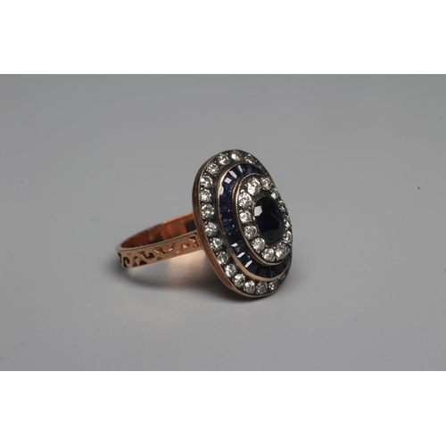 324 - A SAPPHIRE AND DIAMOND DRESS RING, the central oval facet cut sapphire within a border of twelve rou... 