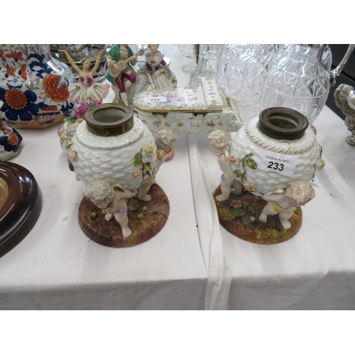 233 - A pair of German porcelain oil lamp reservoirs in the form of cherubs holding up a basket